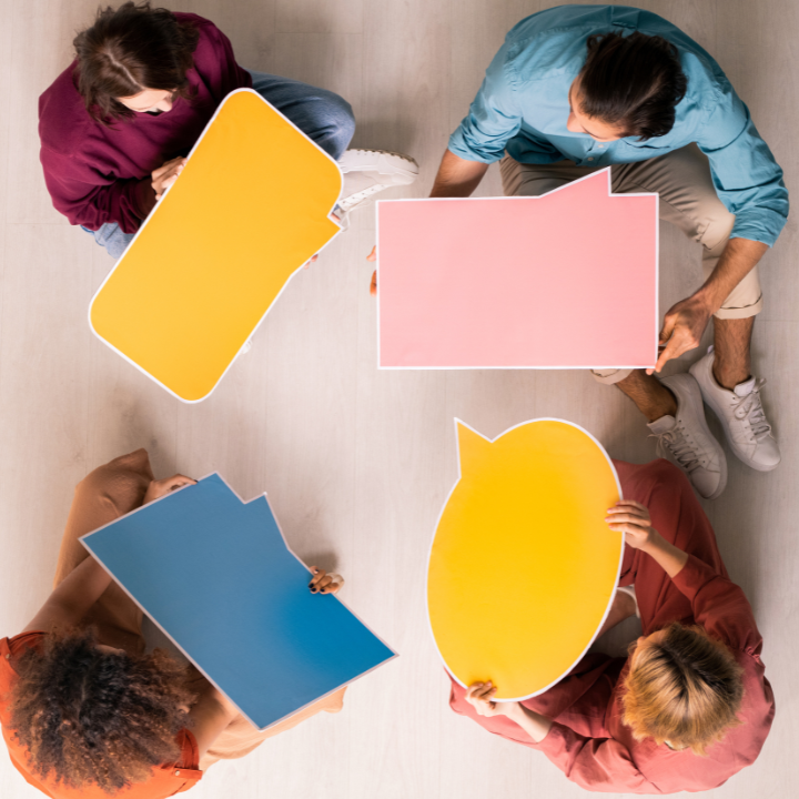 Four people sat in a circle with blank speech bubble cardboard cut outs